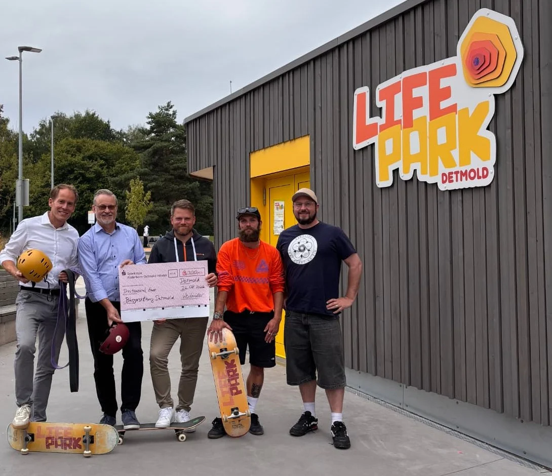 ScheckĂĽbergabe im Life Park Detmold: Vertreter von WeidmĂĽller, BĂĽrgerstiftung Detmold und LIPslide Skateboarding e.V. mit Skateboards vor dem Sport-Pavillon mit dem Life-Park-Logo.